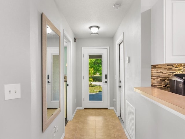 entryway featuring light tile patterned floors, visible vents, a textured ceiling, and baseboards