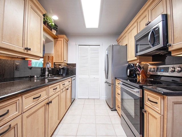 kitchen with a sink, backsplash, light brown cabinetry, appliances with stainless steel finishes, and light tile patterned floors
