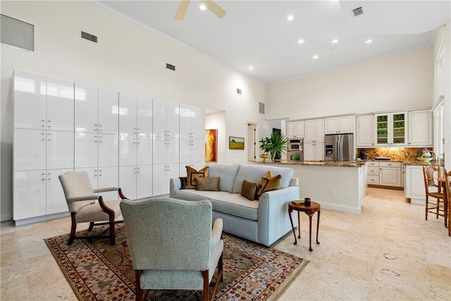 living room with a high ceiling, crown molding, and ceiling fan