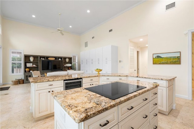 kitchen with black electric cooktop, light stone counters, beverage cooler, and a kitchen island