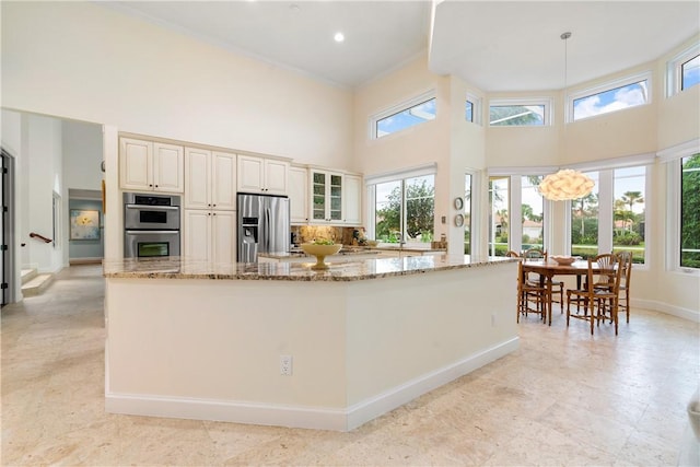 kitchen with appliances with stainless steel finishes, decorative light fixtures, light stone countertops, and a high ceiling