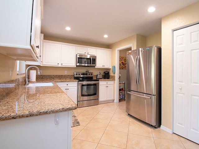 kitchen featuring white cabinetry, sink, appliances with stainless steel finishes, light stone countertops, and light tile patterned floors