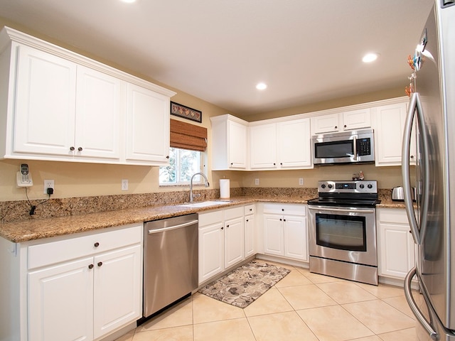 kitchen with light stone counters, light tile patterned flooring, stainless steel appliances, white cabinetry, and sink