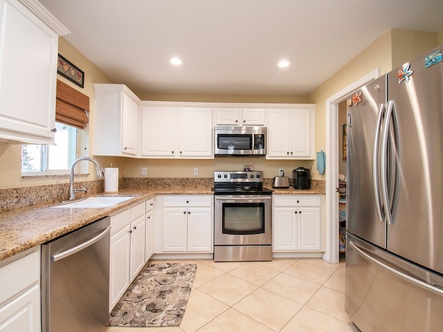 kitchen featuring light stone counters, white cabinets, sink, light tile patterned floors, and appliances with stainless steel finishes