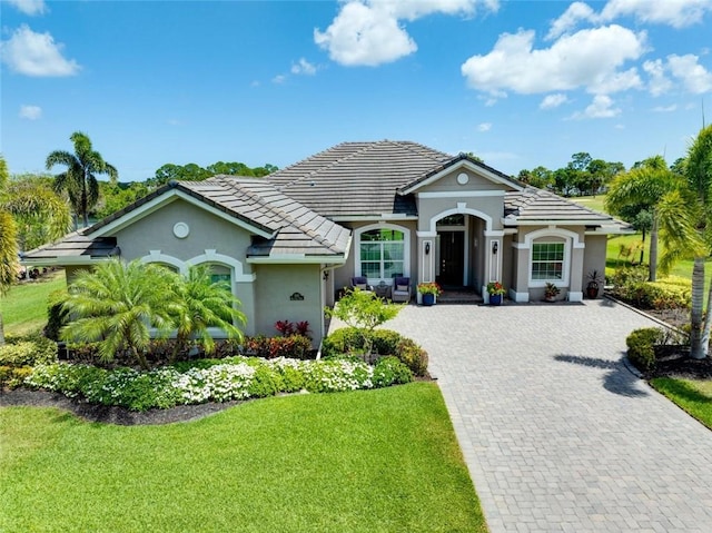 view of front of house featuring stucco siding, decorative driveway, a tiled roof, and a front lawn