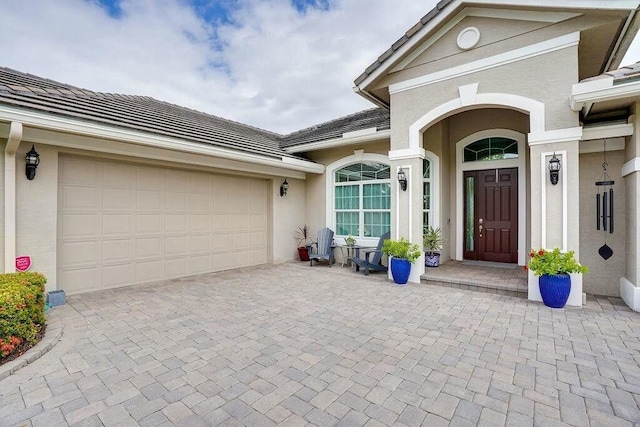 entrance to property with an attached garage, a tile roof, decorative driveway, and stucco siding