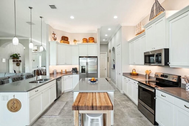 kitchen with arched walkways, crown molding, stainless steel appliances, a sink, and a kitchen island