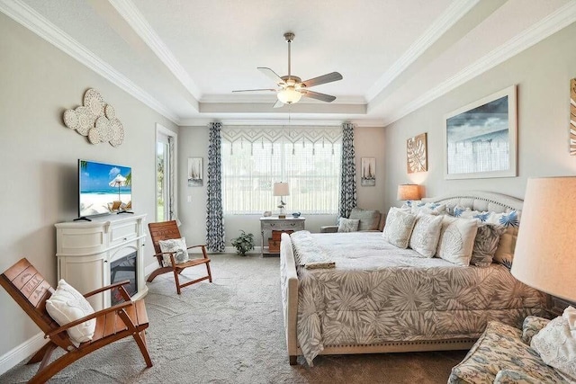 carpeted bedroom featuring ornamental molding, a glass covered fireplace, a raised ceiling, and baseboards