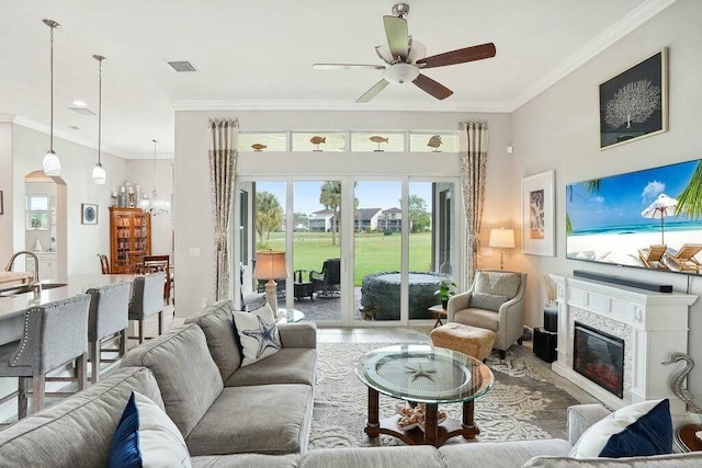 living area featuring a glass covered fireplace, visible vents, crown molding, and ceiling fan