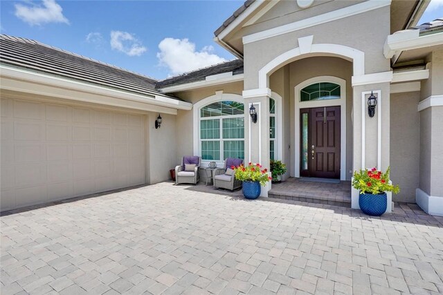 property entrance featuring a tile roof, decorative driveway, stucco siding, and an attached garage