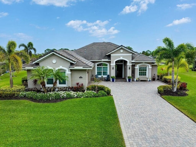 view of front of house with a tiled roof, a front lawn, decorative driveway, and stucco siding