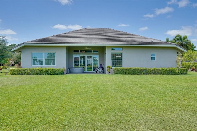 rear view of property featuring stucco siding, a ceiling fan, a yard, and a tiled roof