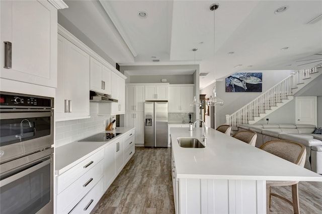 kitchen featuring a center island with sink, appliances with stainless steel finishes, hanging light fixtures, a breakfast bar, and sink