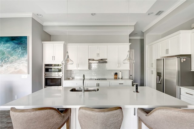 kitchen with hanging light fixtures, stainless steel appliances, a kitchen island with sink, white cabinetry, and sink