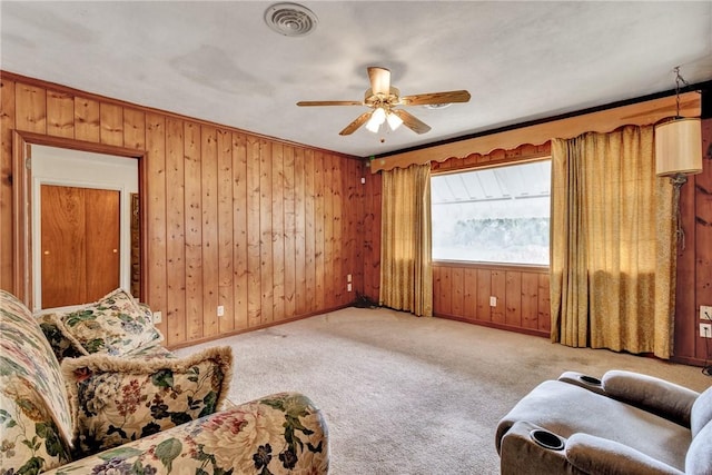 living area featuring carpet flooring, ceiling fan, crown molding, and wood walls