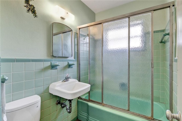 full bathroom featuring sink, toilet, bath / shower combo with glass door, and tile walls