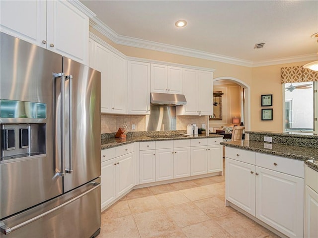 kitchen with white cabinetry, high end refrigerator, crown molding, and dark stone countertops