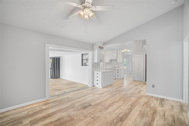 unfurnished living room featuring lofted ceiling, ceiling fan with notable chandelier, a textured ceiling, and light wood-type flooring