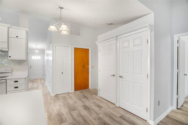 kitchen with pendant lighting, white cabinets, a textured ceiling, and light hardwood / wood-style flooring