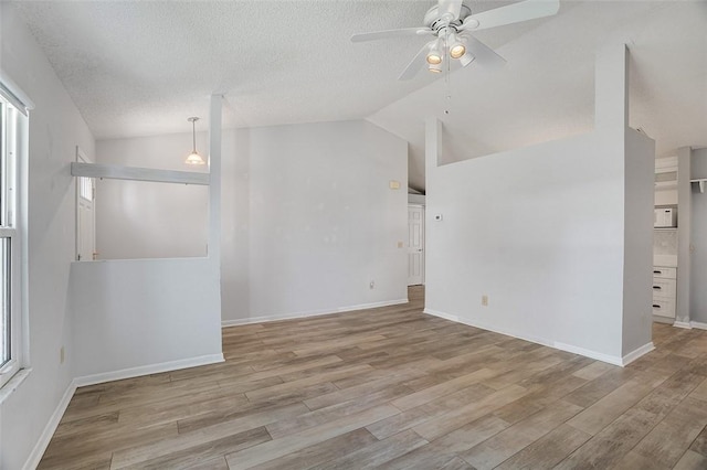 unfurnished room featuring lofted ceiling, plenty of natural light, a textured ceiling, and light hardwood / wood-style flooring