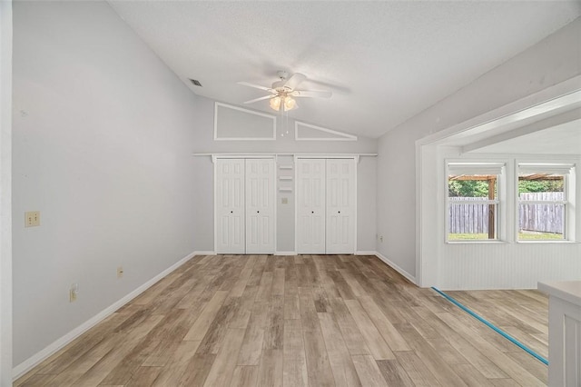 unfurnished bedroom with lofted ceiling, a textured ceiling, multiple closets, ceiling fan, and light hardwood / wood-style floors