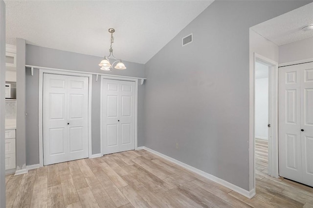 unfurnished bedroom with a chandelier, vaulted ceiling, a textured ceiling, and light wood-type flooring