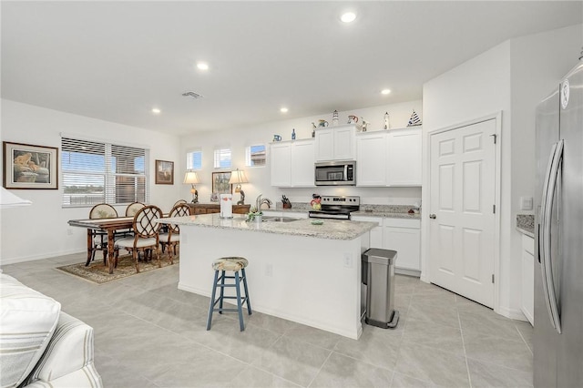 kitchen featuring a center island with sink, white cabinets, sink, appliances with stainless steel finishes, and a kitchen bar