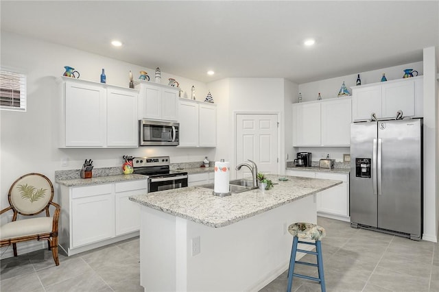 kitchen with a kitchen island with sink, sink, appliances with stainless steel finishes, light stone counters, and white cabinetry