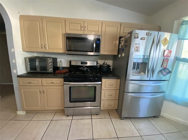 kitchen featuring appliances with stainless steel finishes, light tile patterned floors, lofted ceiling, and light brown cabinetry