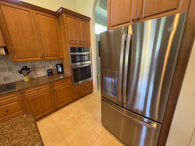 1274 River Reach Dr, Vero Beach, FL 32967 - kitchen with appliances with stainless steel finishes, arched walkways, decorative backsplash, brown cabinetry, and dark stone counters