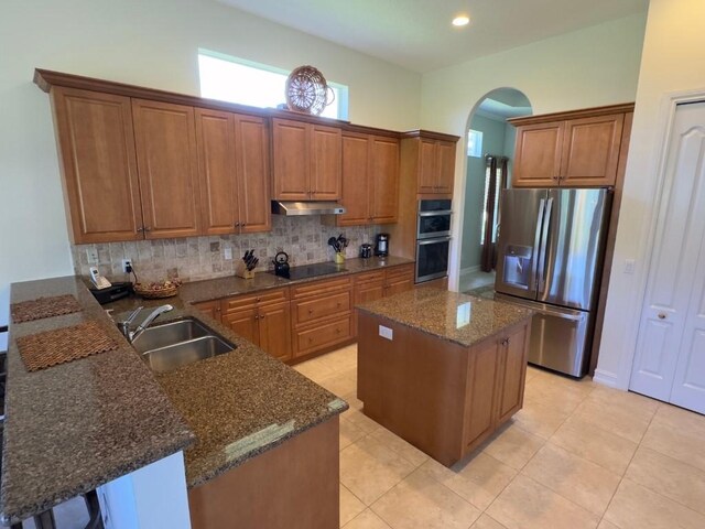 1274 River Reach Dr, Vero Beach, FL 32967 - kitchen with stainless steel appliances, arched walkways, under cabinet range hood, brown cabinets, and decorative backsplash