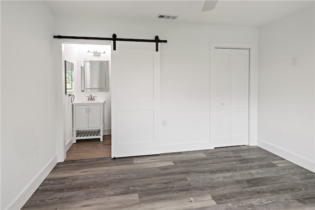 unfurnished bedroom featuring a barn door, sink, dark hardwood / wood-style floors, ceiling fan, and a closet