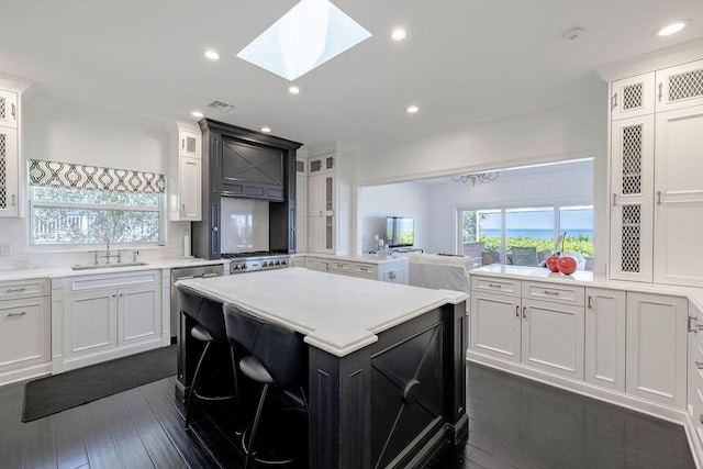 kitchen featuring a center island, a sink, a skylight, glass insert cabinets, and light countertops