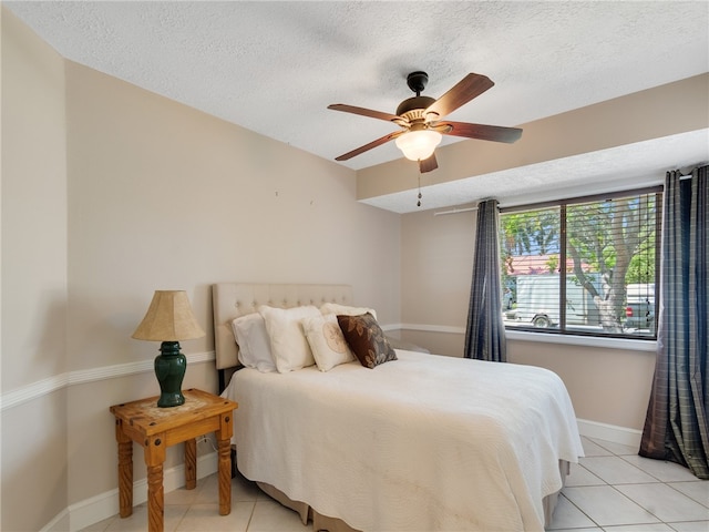 bedroom featuring baseboards, a ceiling fan, a textured ceiling, and light tile patterned floors