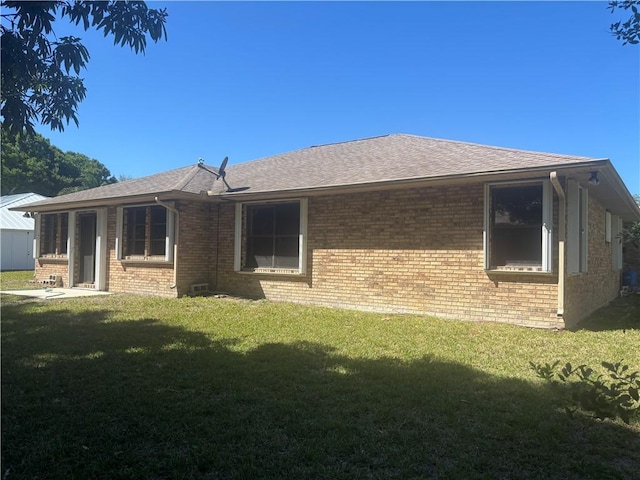 back of house featuring brick siding, a yard, and roof with shingles