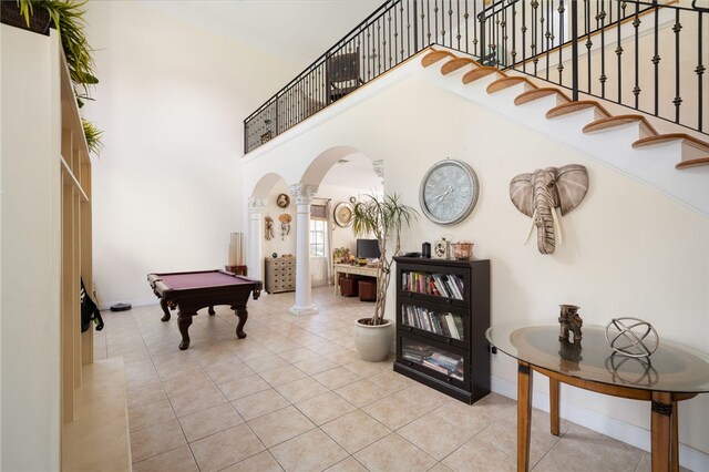 entryway featuring light tile patterned flooring, pool table, ornate columns, and a towering ceiling