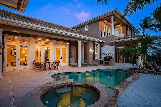 back house at dusk featuring a patio area, french doors, a balcony, and a pool with hot tub