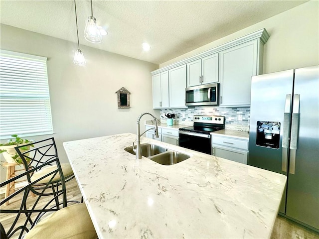 kitchen with sink, pendant lighting, a textured ceiling, a center island with sink, and appliances with stainless steel finishes