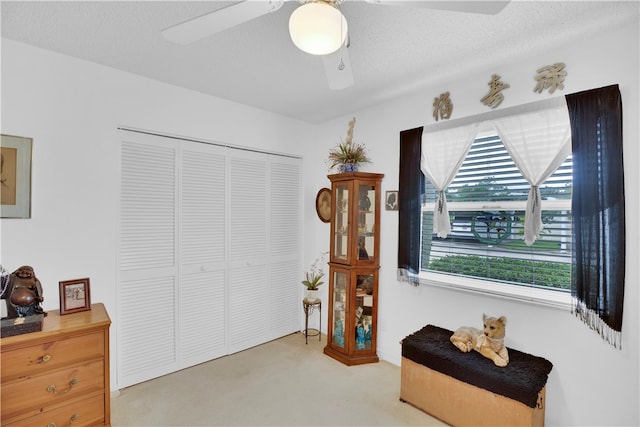 living area with light carpet, ceiling fan, and a textured ceiling