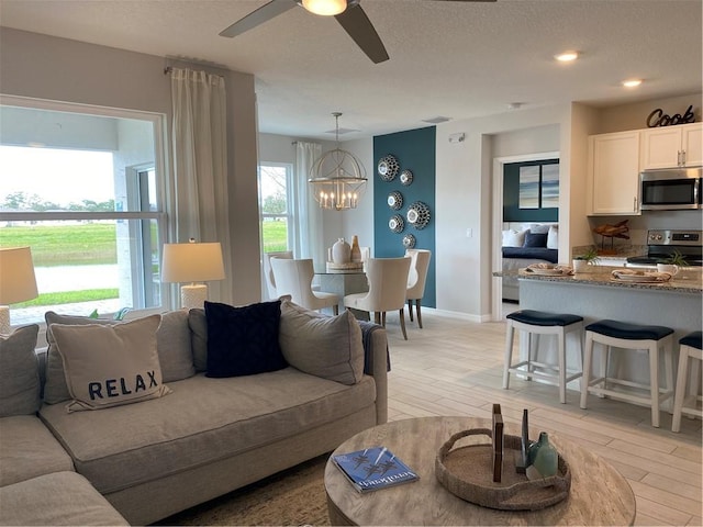 living room featuring ceiling fan with notable chandelier, light hardwood / wood-style floors, and a textured ceiling