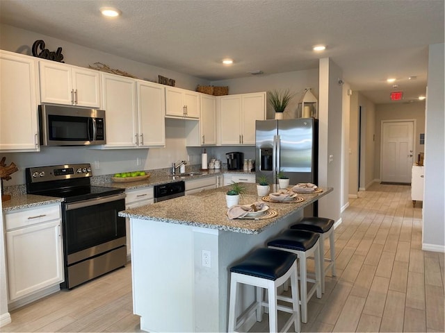 kitchen with a kitchen island, appliances with stainless steel finishes, white cabinets, light stone countertops, and light hardwood / wood-style flooring