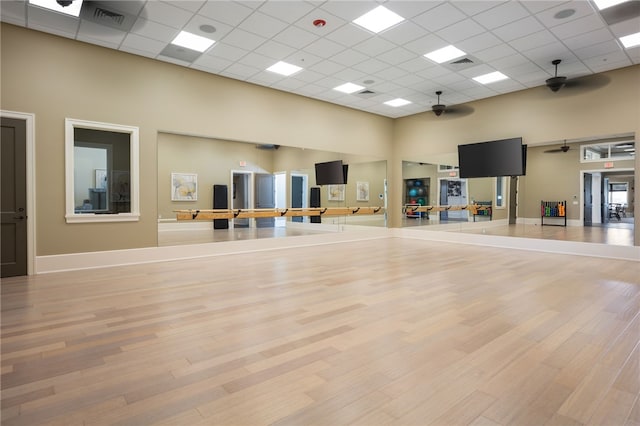 workout room with ceiling fan, a drop ceiling, a high ceiling, and light wood-type flooring