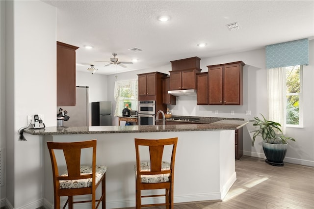 kitchen featuring kitchen peninsula, appliances with stainless steel finishes, a healthy amount of sunlight, and dark stone countertops