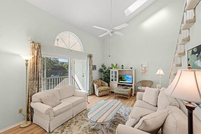 living room with ceiling fan, light hardwood / wood-style floors, high vaulted ceiling, and a skylight