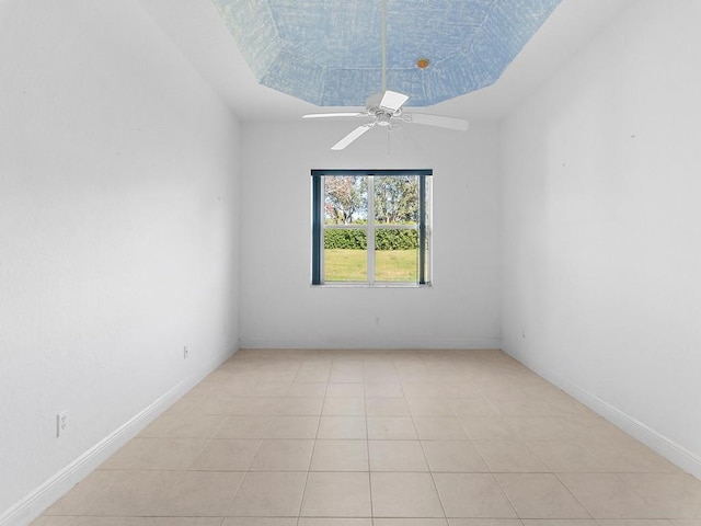 tiled empty room featuring a raised ceiling and ceiling fan