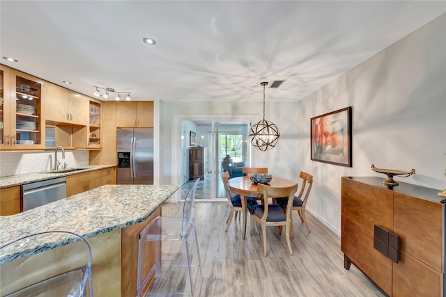 kitchen with appliances with stainless steel finishes, sink, a breakfast bar area, hanging light fixtures, and light stone counters