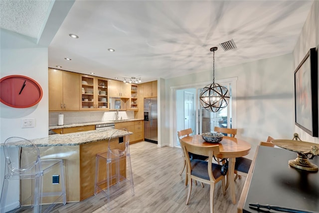 kitchen featuring a kitchen bar, sink, light stone counters, pendant lighting, and stainless steel appliances