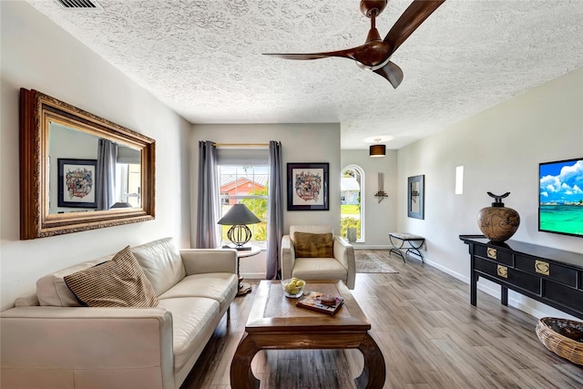 living room with a textured ceiling, ceiling fan, and light hardwood / wood-style flooring