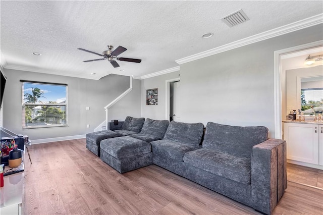 living room with ceiling fan, light wood-type flooring, a textured ceiling, and ornamental molding