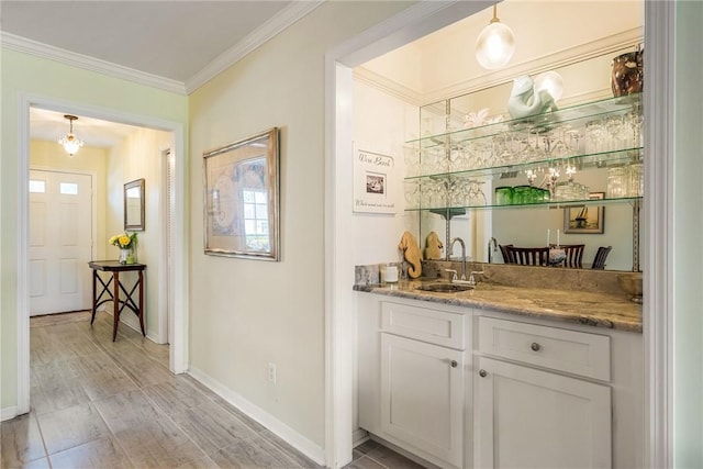 bar with hanging light fixtures, ornamental molding, sink, and white cabinets